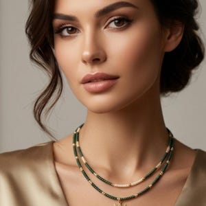 Puede incluir: Collar de varias capas con un colgante de sol y luna dorado. El collar presenta cuentas verdes oscuras y doradas, con una hebra de cuentas blancas. El colgante es un diseño detallado de sol y luna creciente, con acabado dorado.