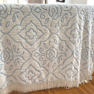 May include: A white and light blue throw blanket with a floral pattern and fringe trim.