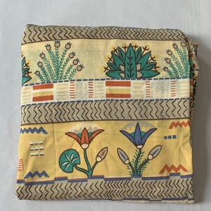 May include: A folded piece of fabric with a yellow background and a repeating pattern of stylized flowers and geometric designs in shades of blue, green, orange, and brown.