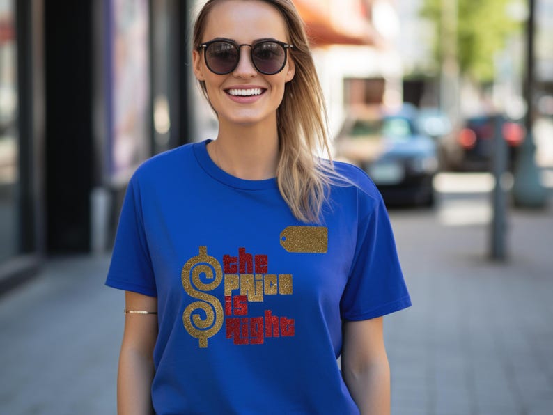 May include: A royal blue short-sleeved t-shirt featuring a large gold glitter dollar sign and the text "the price is right" in red and gold glitter lettering. A small gold glitter rectangular tag icon is positioned above the text.