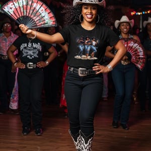 Op de afbeelding: Een vrouw draagt een cowboyhoed en een zwart t-shirt met een afbeelding van drie vrouwen in jeans. Ze houdt een rood-zwarte waaier vast. Andere mensen met cowboyhoeden en zwarte shirts zijn op de achtergrond.