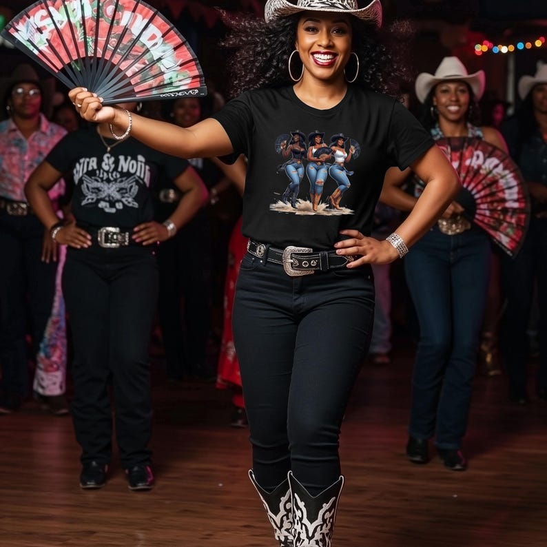 Op de afbeelding: Een vrouw draagt een cowboyhoed en een zwart t-shirt met een afbeelding van drie vrouwen in jeans. Ze houdt een rood-zwarte waaier vast. Andere mensen met cowboyhoeden en zwarte shirts zijn op de achtergrond.