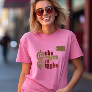 May include: A short-sleeved pink t-shirt featuring a gold glitter dollar sign, a gold glitter price tag icon, and the text "the PRICE is Right" in red and gold glitter lettering printed on the front of the garment.