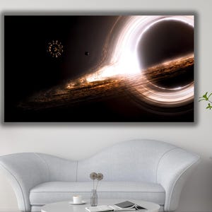 Może przedstawiać: Duży wydruk na płótnie przedstawiający czarną dziurę w kosmosie. Grafika przedstawia jasny, świecący pierścień wokół ciemnego środka, z wirującymi galaktykami w odcieniach brązu i złota. Widoczny jest również obiekt niebieski.