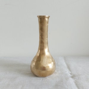 May include: A gold metal vase with a hammered finish. The vase has a round base and a narrow neck.