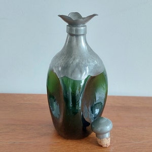 May include: A green glass bottle with a pewter top and a flower-shaped spout. The bottle has a textured surface and a cork stopper.