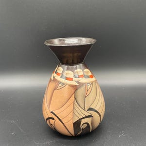 Puede incluir: Un jarrón de cerámica marrón con un diseño geométrico en tonos marrones, beige, negro y rojo. El jarrón tiene una boca ancha y un cuello estrecho.