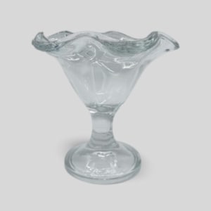 May include: Clear glass sundae dish with a ruffled rim. The bowl is supported by a stem and a circular base. The glass has a transparent appearance, and the design is simple and elegant. Ideal for serving ice cream or desserts.