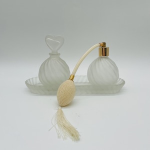 May include: A frosted glass perfume bottle set with a heart-shaped stopper and a spray bottle with a white tassel. The bottles are on a frosted glass tray.