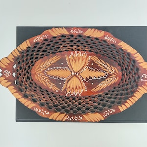 May include: An oval wooden serving tray with a lattice design and painted floral details. The tray is brown with white and light brown accents.