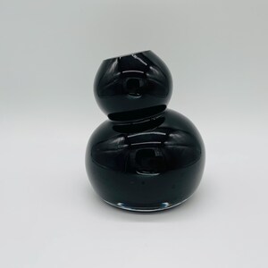 May include: A striking black glass vase with a distinctive stacked form. The vase has a spherical base and a smaller, rounded top, forming an eye-catching shape. The top opening is angled, giving a contemporary feel to the decorative item.