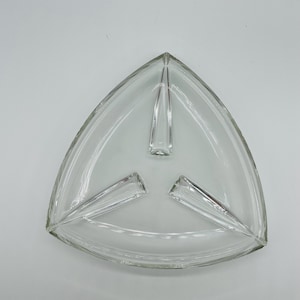 Op de afbeelding: Driehoekige serveerschaal van helder glas met drie compartimenten. De schaal heeft een glad oppervlak en een opstaande rand. De compartimenten worden gescheiden door verhoogde verdelers. Ideaal voor het serveren van hapjes of snacks.