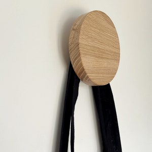 May include: A wooden wall hook with a round, light brown, wood grain design. A black tote bag is hanging from the hook.