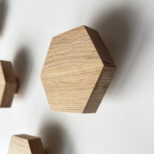 May include: Four wooden hexagonal hooks mounted on a white wall. The hooks are made of light brown wood and have a natural finish.