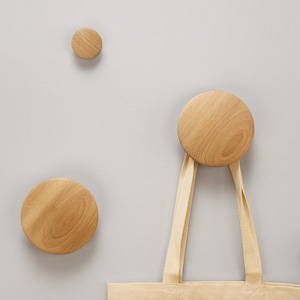 May include: A beige tote bag hanging on a wooden wall hook. The hook is a round wooden knob. There are two other wooden knobs on the wall.