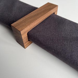 Puede incluir: Una taza de cerámica blanca con un asa negra y el texto "But First, Coffee" en negrita negra. La taza se encuentra sobre un fondo neutro, resaltando su diseño simple.