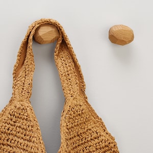 Puede incluir: Un bolso tote tejido marrón colgado de un gancho de madera. El gancho tiene forma de roca redondeada.