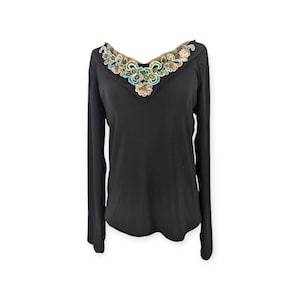 Può includere: Maglia nera a maniche lunghe con scollo a V. Lo scollo è impreziosito da un motivo floreale decorativo nei toni dell'oro, del verde e del blu. La maglia è realizzata in un materiale morbido e confortevole.