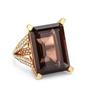 Könnte beinhalten: Ein goldener Ring mit einem großen, rechteckigen, dunkelbraunen Edelstein und einem mit Diamanten besetzten Band.