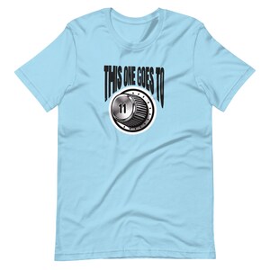 Könnte beinhalten: Hellblaues T-Shirt mit dem Text "THIS ONE GOES TO" über einer Grafik eines silbernen Lautstärkereglers mit der Zahl 11. Das T-Shirt hat einen Rundhalsausschnitt und kurze Ärmel.