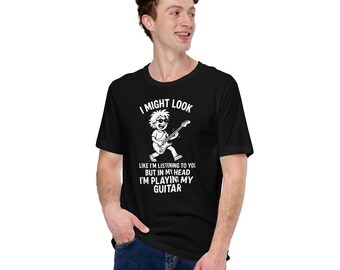 May include: Black t-shirt with the text "I MIGHT LOOK LIKE I'M LISTENING TO YOU BUT IN MY HEAD I'M PLAYING MY GUITAR" and a white graphic of a person playing a guitar. The shirt is worn by a person.