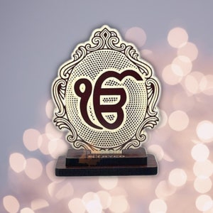May include: A wooden decorative stand with a gold and brown finish. The stand features a circular design with a brown "Ek Onkar" symbol in the centre. The symbol is surrounded by a dotted pattern and a decorative frame.