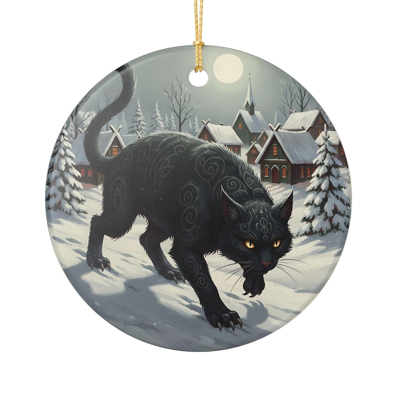 May include: A round ceramic ornament featuring a black cat with intricate silver swirl patterns on its fur, yellow eyes, and a raised tail. The cat stands in a snowy village scene with pine trees, small houses, and a full moon in the background.
