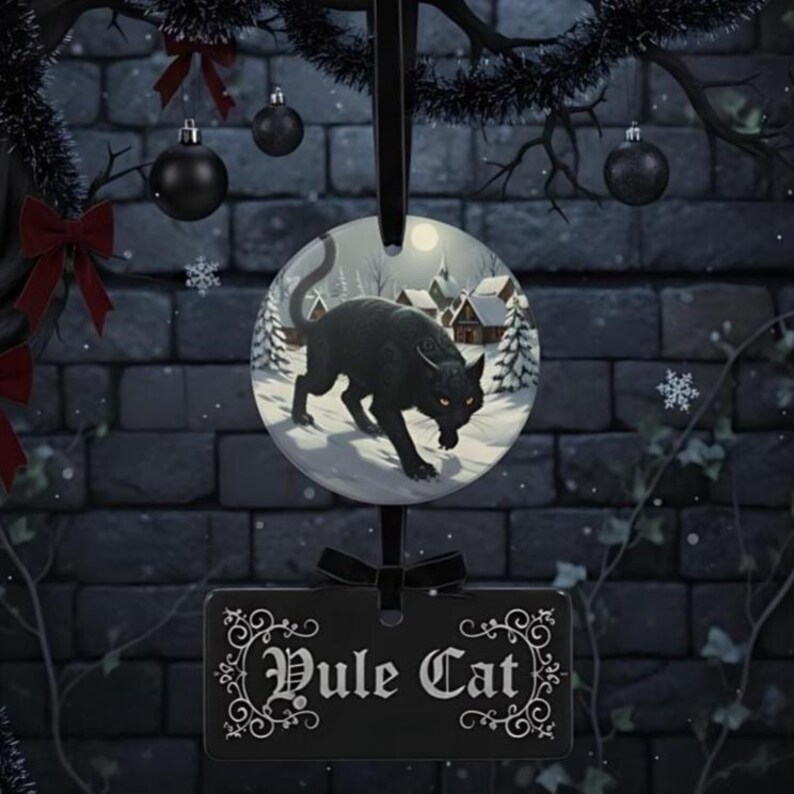 May include: A circular ceramic ornament featuring a black cat in a snowy village scene, suspended above a rectangular black plaque with white decorative scrollwork borders and the text Yule Cat written in a stylized gothic font.