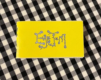 May include: A small, rectangular yellow notebook with the word "Eye Jam" in blue, stylized lettering. The notebook is set against a black and white checkered background.