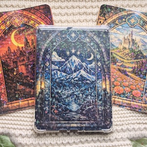 May include: Three decorative tablet cases with stained glass designs. The center case features a mountain landscape under a starry sky. The other two cases have castle and city scenes with arched frames, in shades of orange, red, and blue.
