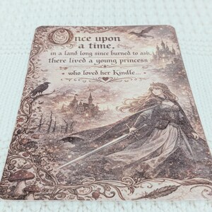 May include: A decorative card with a fantasy illustration. The card features a princess holding a sword, a castle, and the text "Once upon a time... who loved her Kindle." The color palette is sepia tones.