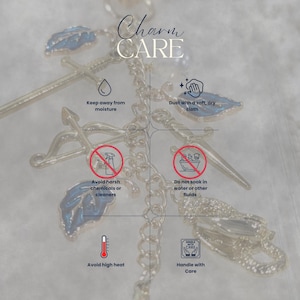 May include: A close-up of a silver-colored charm with blue leaf accents and a chain. The image includes text that reads "Charm CARE" and instructions: "Keep away from moisture," "Dust with a soft, dry cloth," and "Avoid harsh chemicals or cleaners."