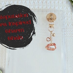 May include: A gold-toned charm chain with heart and lip charms. The charm is attached to a clear phone case. The text on the image says "Reputation Era Inspired Charm Chain."
