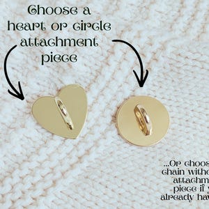 May include: Two gold-colored attachment pieces: a heart and a circle. Each has a loop for attaching a chain. Text above reads "Choose a heart or circle attachment piece." The background is a white, textured fabric.