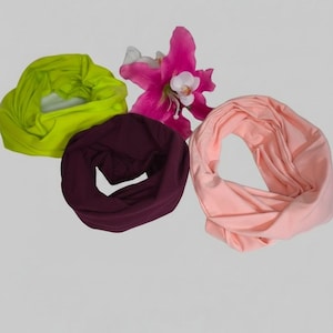Könnte beinhalten: Vier unendliche Schals in den Farbtönen Chartreuse, Burgunderrot und Pfirsich, angeordnet mit einer rosa und weißen Blume. Die Schals sind aus einem weichen, fließenden Stoff gefertigt, ideal, um jedem Outfit einen Farbtupfer zu verleihen.