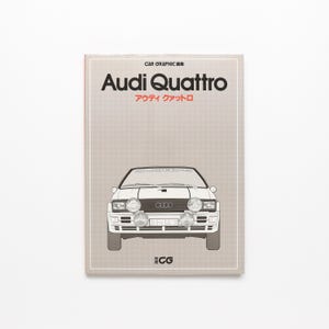 Peut inclure: Une couverture de livre rectangulaire avec un fond quadrillé beige clair présentant un dessin au trait noir et blanc d'une voiture Audi Quattro. Le texte indique CAR GRAPHIC, Audi Quattro, et des caractères japonais en rouge, avec le logo CG.