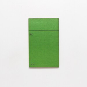 May include: A rectangular, bright green book cover with a horizontal black line near the top. A small, circular emblem with three stick figures is in the upper left corner. The text "DOR 1.30 M" is printed at the bottom.