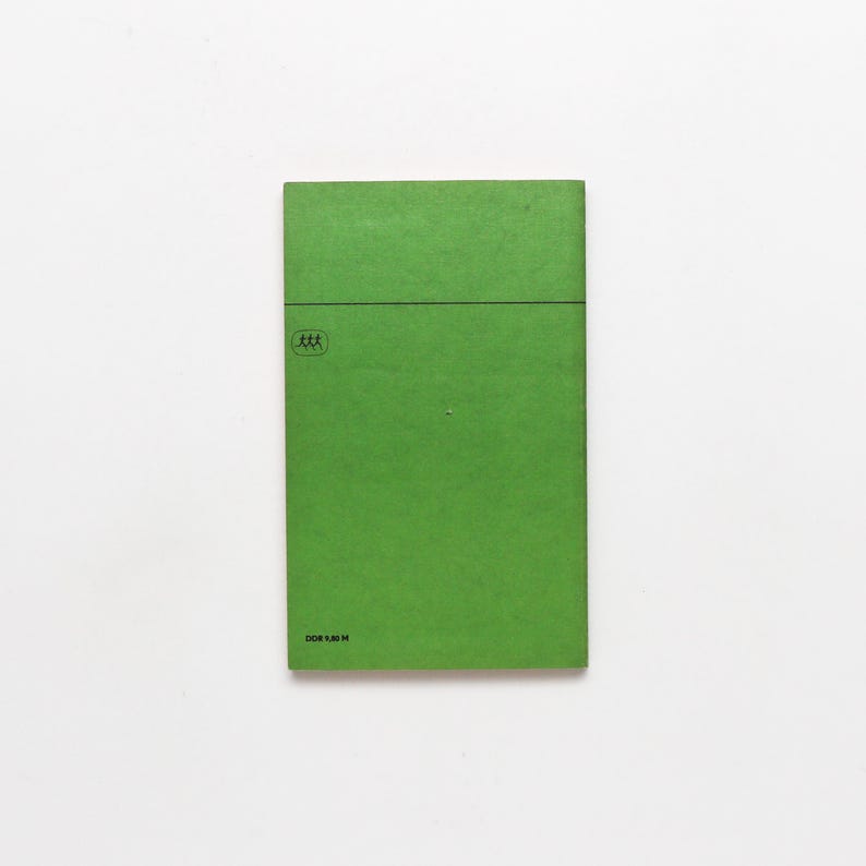 May include: A rectangular, bright green book cover with a horizontal black line near the top. A small, circular emblem with three stick figures is in the upper left corner. The text "DOR 1.30 M" is printed at the bottom.