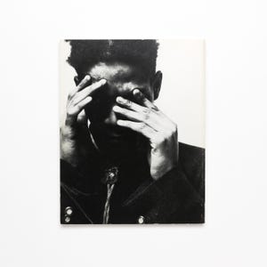 K&ouml;nnte beinhalten: Schwarzwei&szlig;foto einer Person, die sich mit den H&auml;nden das Gesicht bedeckt. Die Person tr&auml;gt eine dunkle Jacke.