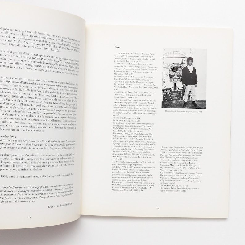 K&ouml;nnte beinhalten: Ein Schwarzwei&szlig;foto eines Mannes, der vor einem gro&szlig;en, farbenfrohen Gem&auml;lde steht. Das Gem&auml;lde zeigt ein gro&szlig;es, abstraktes Gesicht mit einem roten Mund und einem blauen Auge. Der Mann tr&auml;gt ein wei&szlig;es Hemd und eine schwarze Hose. Das Gem&auml;lde ist mit "Philosophie, Jean-Michel Basquiat, 1982" betitelt.