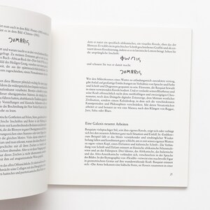 May include: An open book with text and the word "OVMARIS" in bold. The text is likely an essay or article, possibly about art or culture. The pages are white with black text.