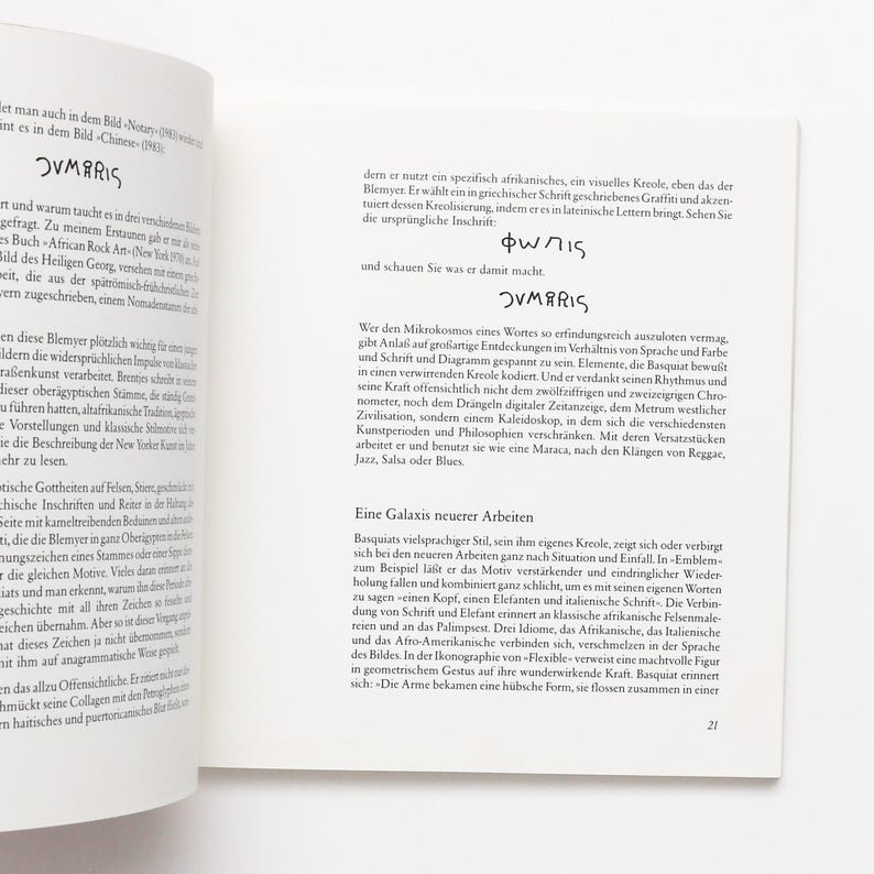 May include: An open book with text and the word "OVMARIS" in bold. The text is likely an essay or article, possibly about art or culture. The pages are white with black text.