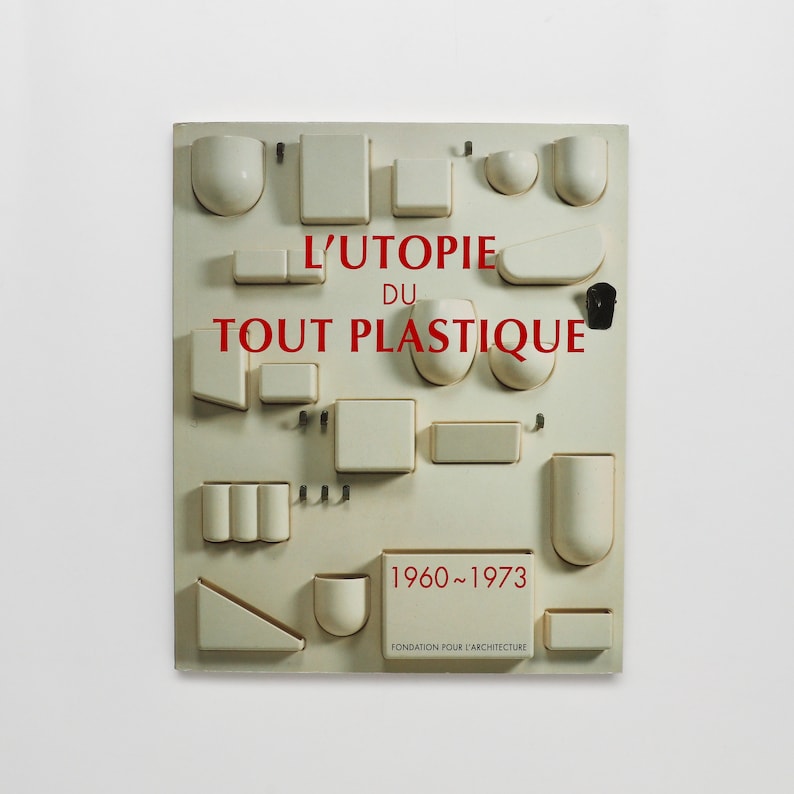May include: A white board with various shapes and sizes of plastic objects arranged in a grid pattern. The board has the text "L'UTOPIE DU TOUT PLASTIQUE 1960-1973" and "FONDATION POUR L'ARCHITECTURE" printed on it.
