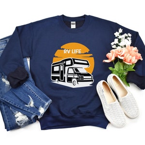 May include: A navy blue sweatshirt with the text "RV LIFE" printed on the front. The sweatshirt features a graphic of a camper van with a sunset behind it.