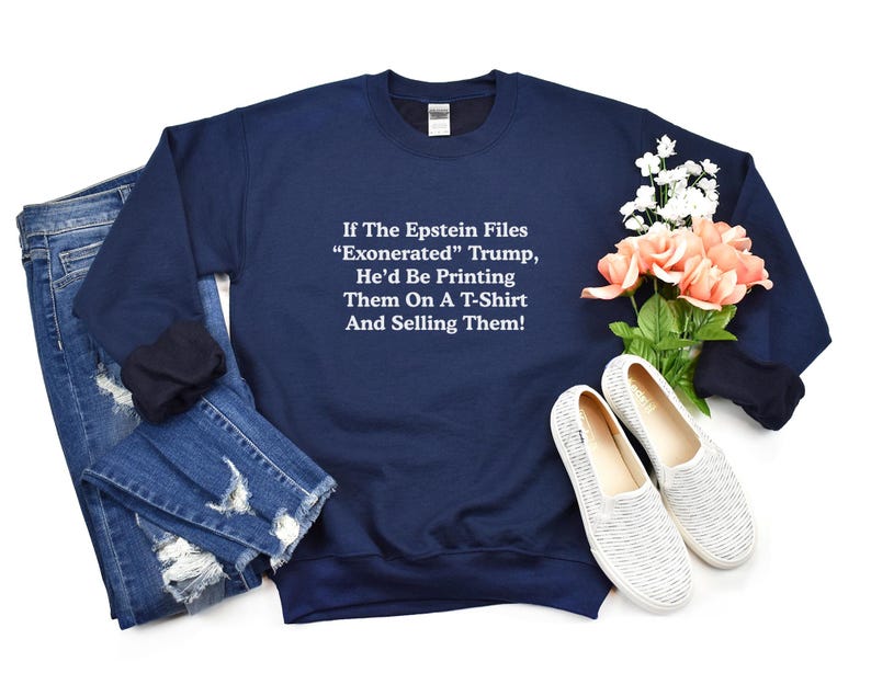 May include: Navy blue sweatshirt with white text: "If The Epstein Files 'Exonerated' Trump, He'd Be Printing Them On A T-Shirt And Selling Them!" The sweatshirt is paired with blue jeans and white shoes with a floral arrangement.