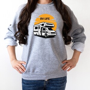 May include: A gray sweatshirt with a graphic of a camper van in front of a yellow sun with the text "RV LIFE" on it.