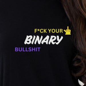 May include: Black t-shirt with the text "F*CK YOUR BINARY BULLSHIT" in white, yellow, and purple. The design includes a yellow hand gesture. The shirt is a statement piece.