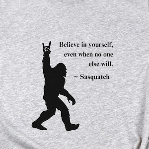 May include: A gray t-shirt with a black silhouette of a Bigfoot with a rock and roll hand gesture. The text reads "Believe in yourself, even when no one else will. ~Sasquatch"