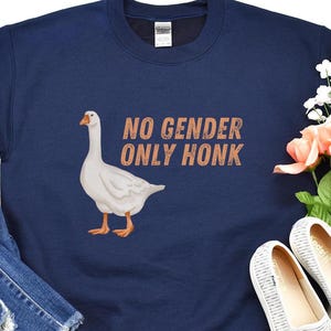 May include: A navy blue sweatshirt with a white goose and the text "NO GENDER ONLY HONK" in orange.