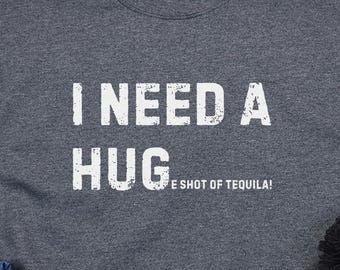May include: A dark gray sweatshirt with the text "I need a hug and a shot of tequila!" printed in white.